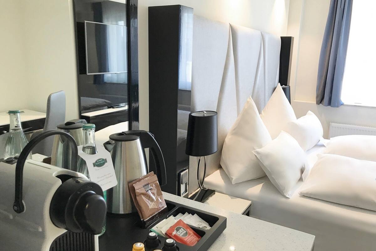 Une chambre d’hôtel avec un lit, un bureau équipé d’une machine à café, d’une bouilloire et d’un plateau avec des sachets de café.