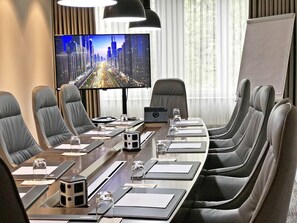 A conference room with a long table, multiple chairs, a large screen, and a whiteboard.