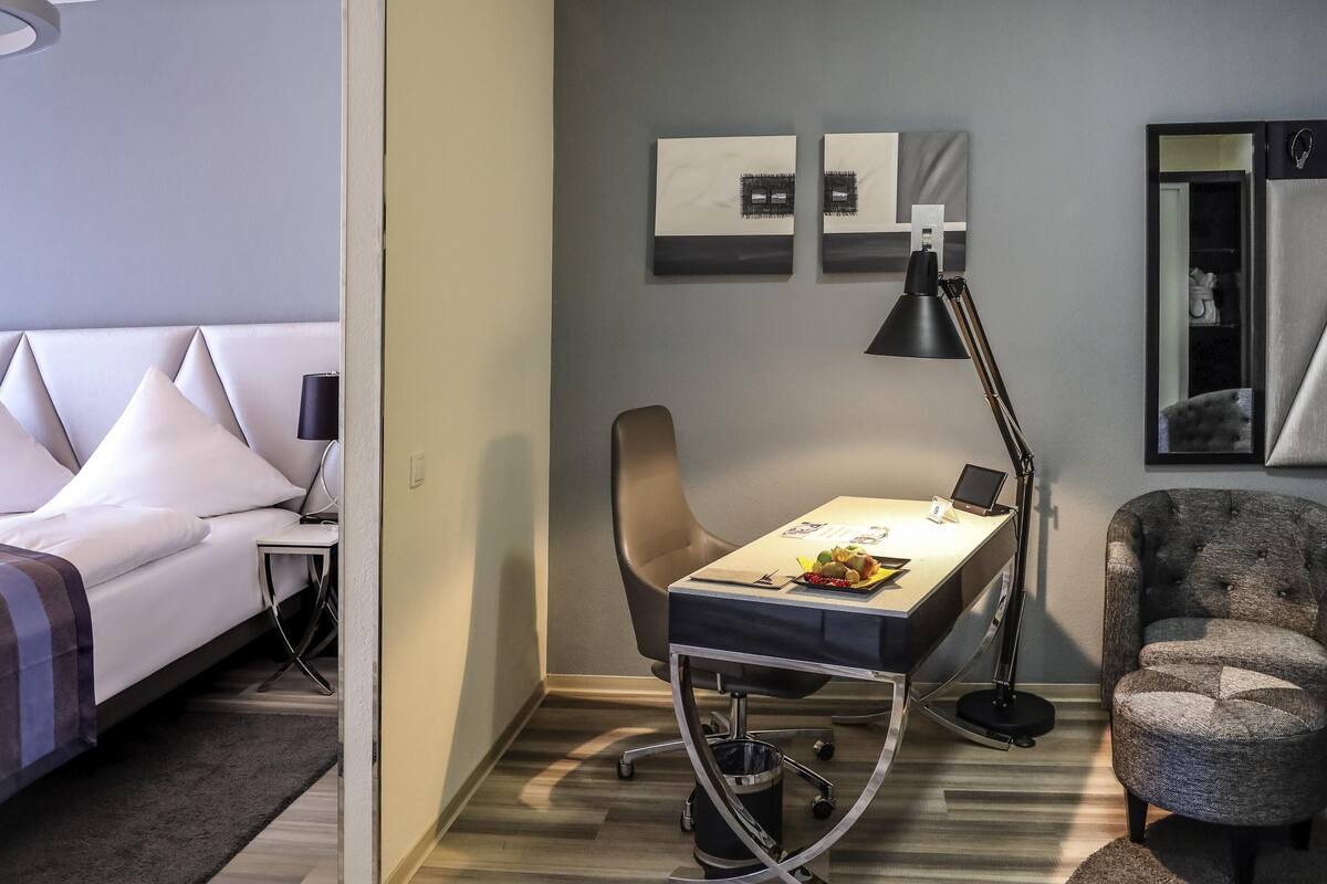 Une chambre d’hôtel avec un lit, un bureau et une chaise, une lampe et des œuvres d’art accrochées au mur.