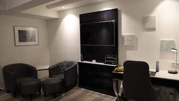 A modern room with a large black entertainment unit, two grey armchairs, a desk with a computer, and a small rug.
