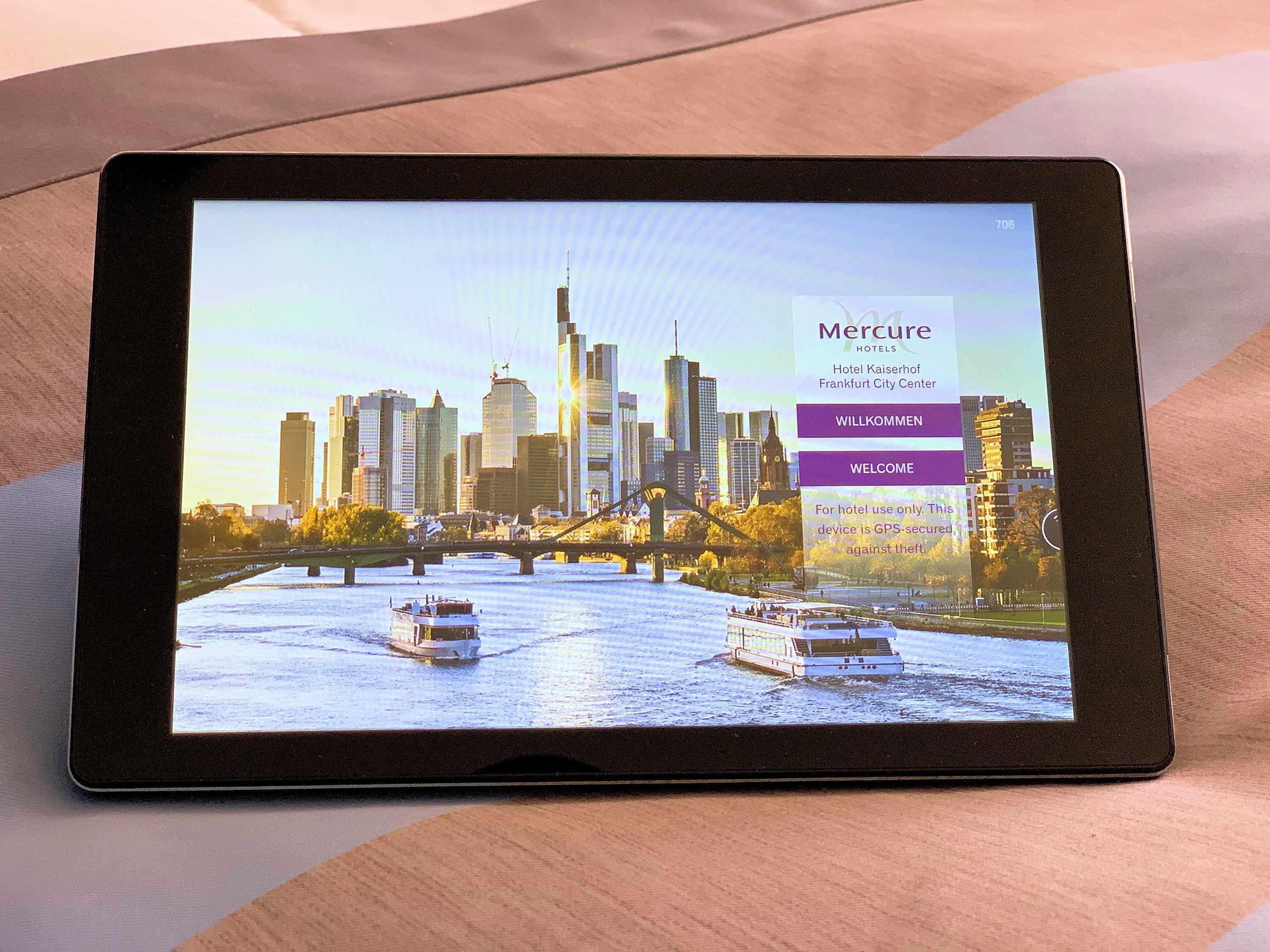 Una tableta muestra un sitio web de hotel con un fondo de horizonte urbano, destacando el Hotel Kaiserhof en el centro de Frankfurt.