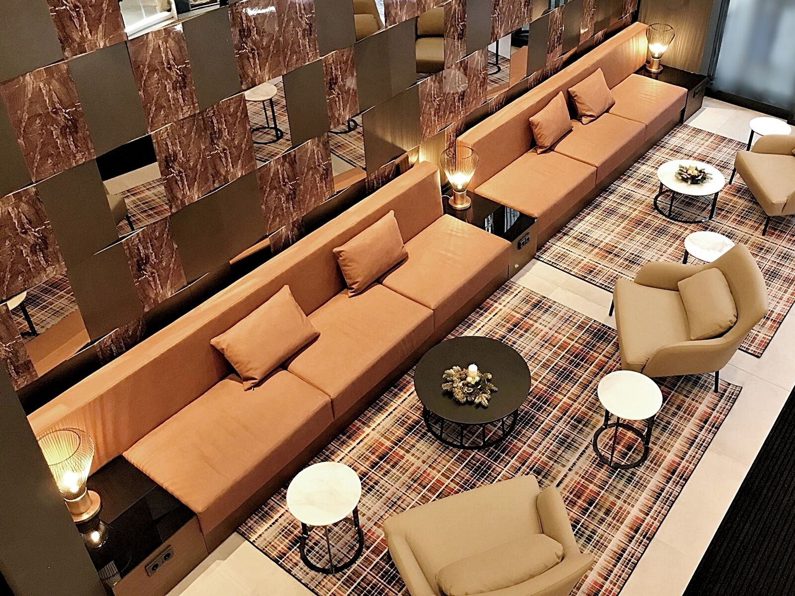 A modern lounge area with a long sofa, armchairs, and small tables.