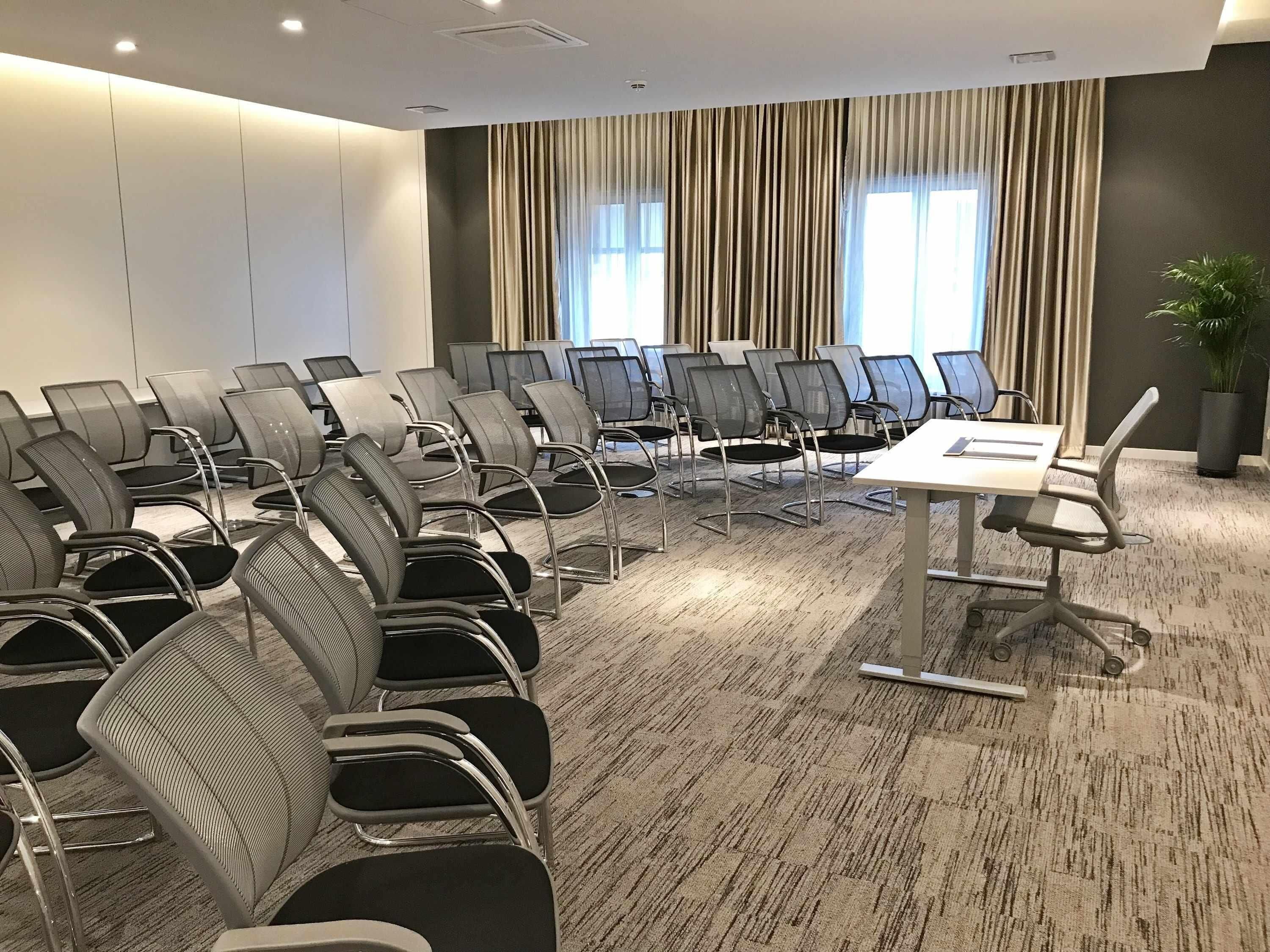 Une salle de conférence avec des rangées de chaises, une table et une plante en pot.