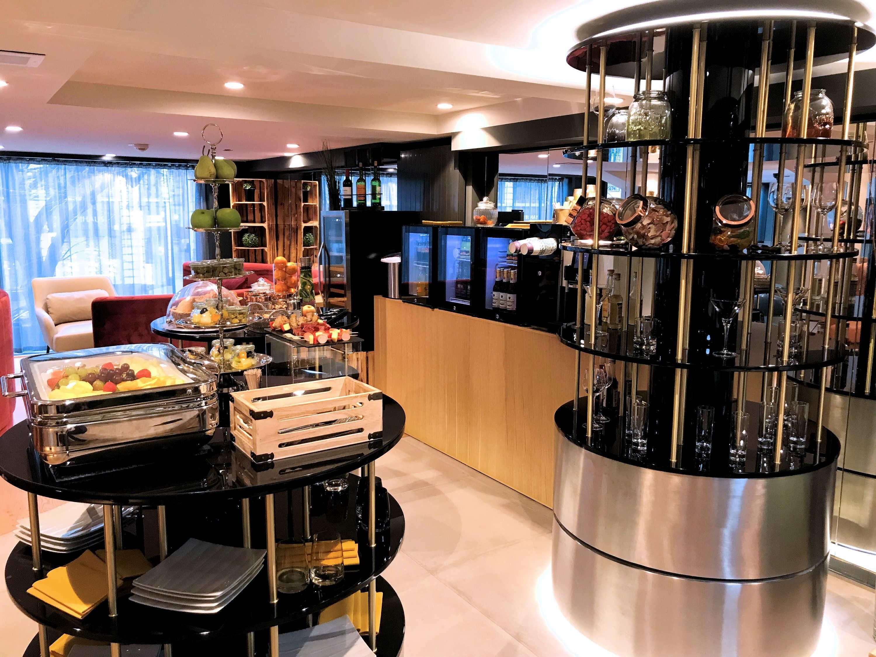 A modern hotel room with a round black table, a wooden crate, and a glass container of fruits.