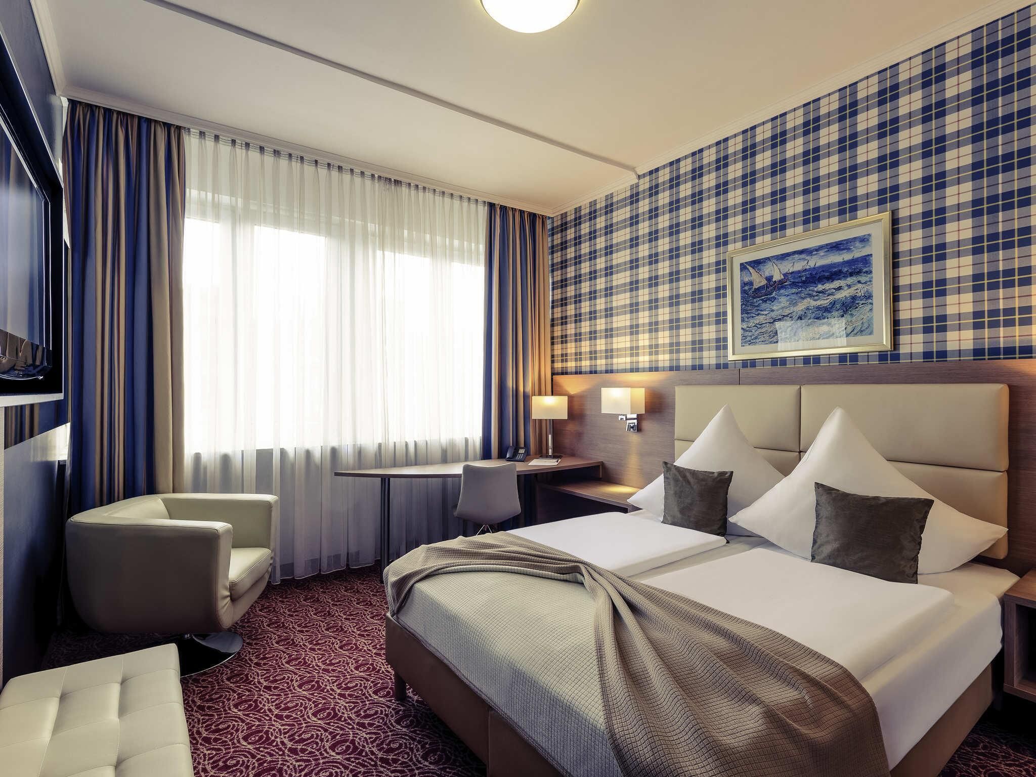 A hotel room with a bed, two bedside tables, a desk, a chair, a television, and a large window with curtains.