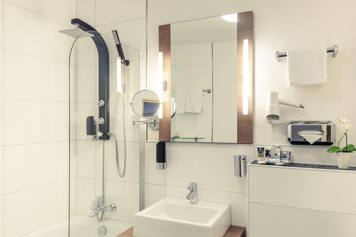 Un baño moderno con ducha de vidrio, un lavamanos, un espejo y un perchero para toallas.