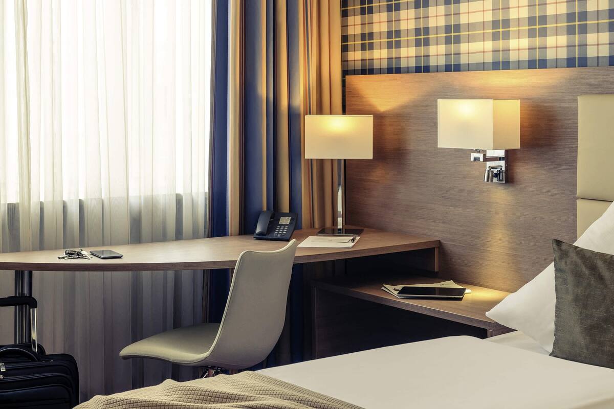 Une chambre d’hôtel équipée d’un bureau, d’une chaise, d’un lit et d’une lampe.