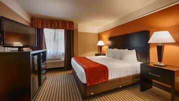 A hotel room with a bed, a TV, two bedside lamps, a desk, and a window with curtains.