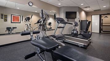 Et fitnesscenter med forskellig træningsudstyr, herunder løbebånd og styrkemaskiner, samt et stort spejl på væggen.