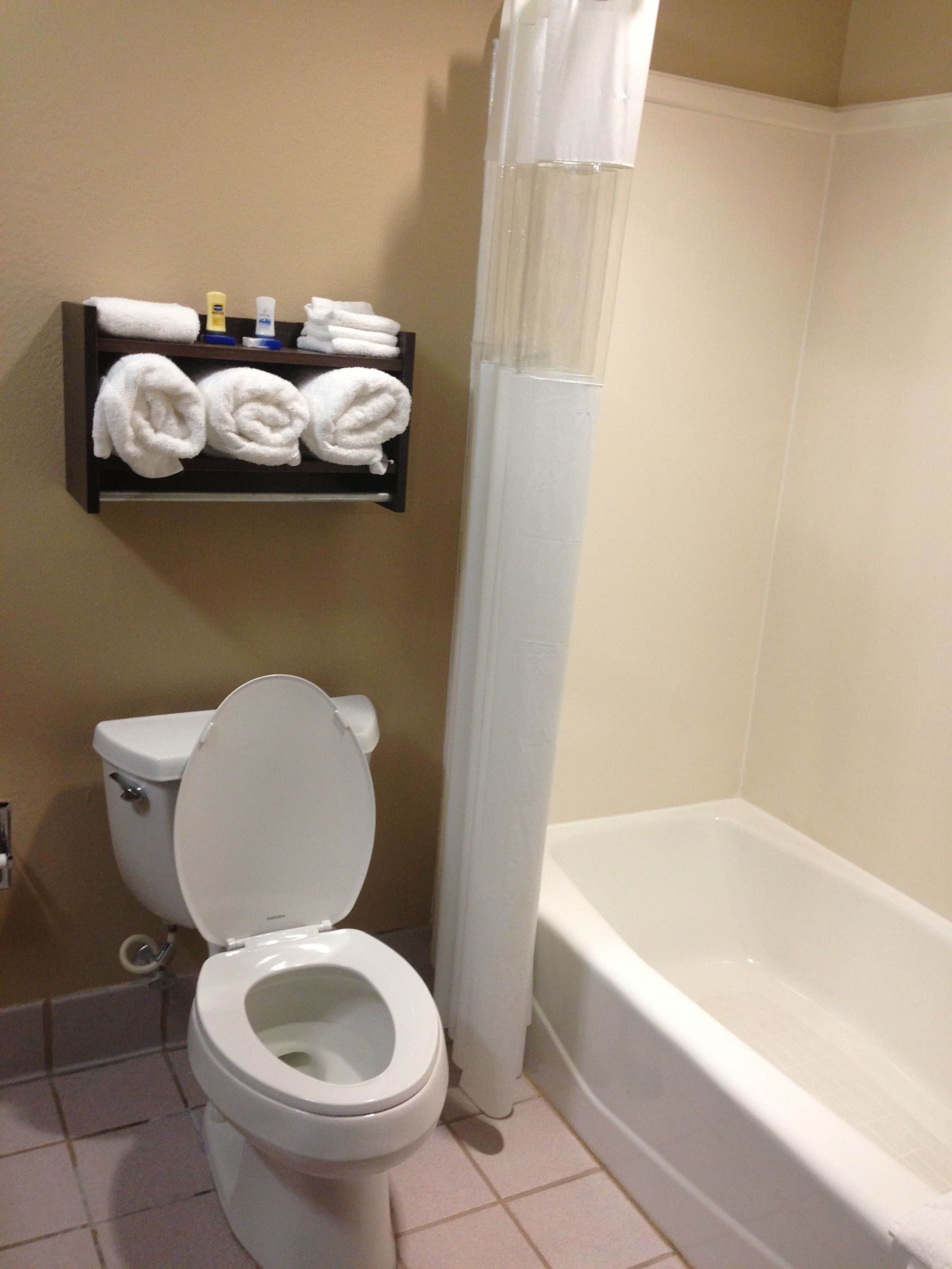 A bathroom with a toilet, a shelf with towels, and a bathtub.