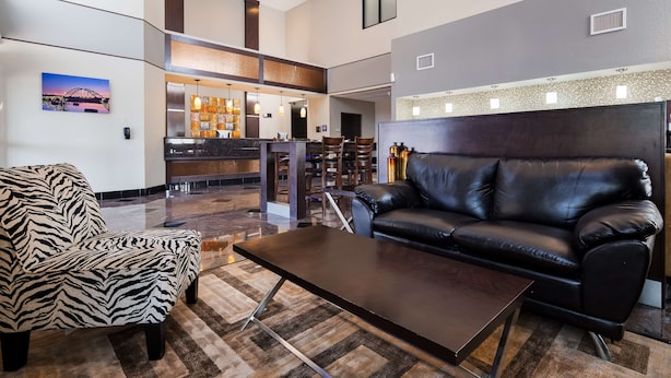 A modern lobby with a black leather sofa, a zebra-patterned armchair, and a wooden coffee table. There is a reception desk with a tiled backsplash and pendant lighting. - Best Western Inn & Suites - Lake Charles (Lake Charles)