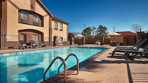 A swimming pool with lounge chairs and umbrellas, surrounded by a brick building with a red roof. - Best Western Inn & Suites - Lake Charles (Lake Charles)