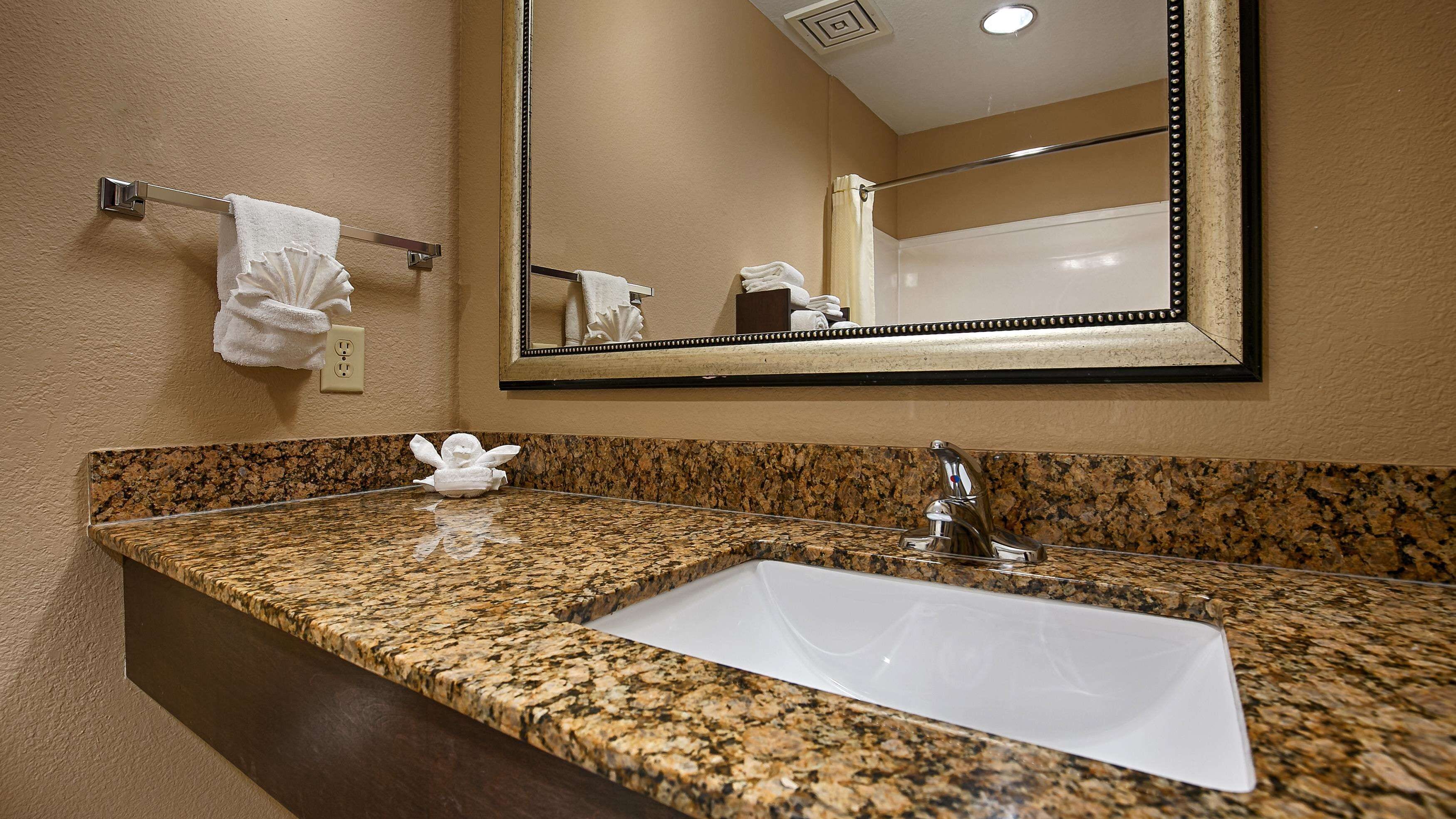 A bathroom with a granite countertop, a white sink, a mirror, and a towel rack.