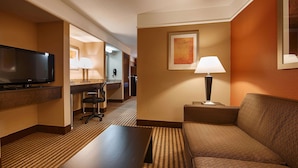 A hotel room with a flat-screen TV, a desk with a lamp, a sofa, and a patterned carpet. - Best Western Inn & Suites - Lake Charles (Lake Charles)