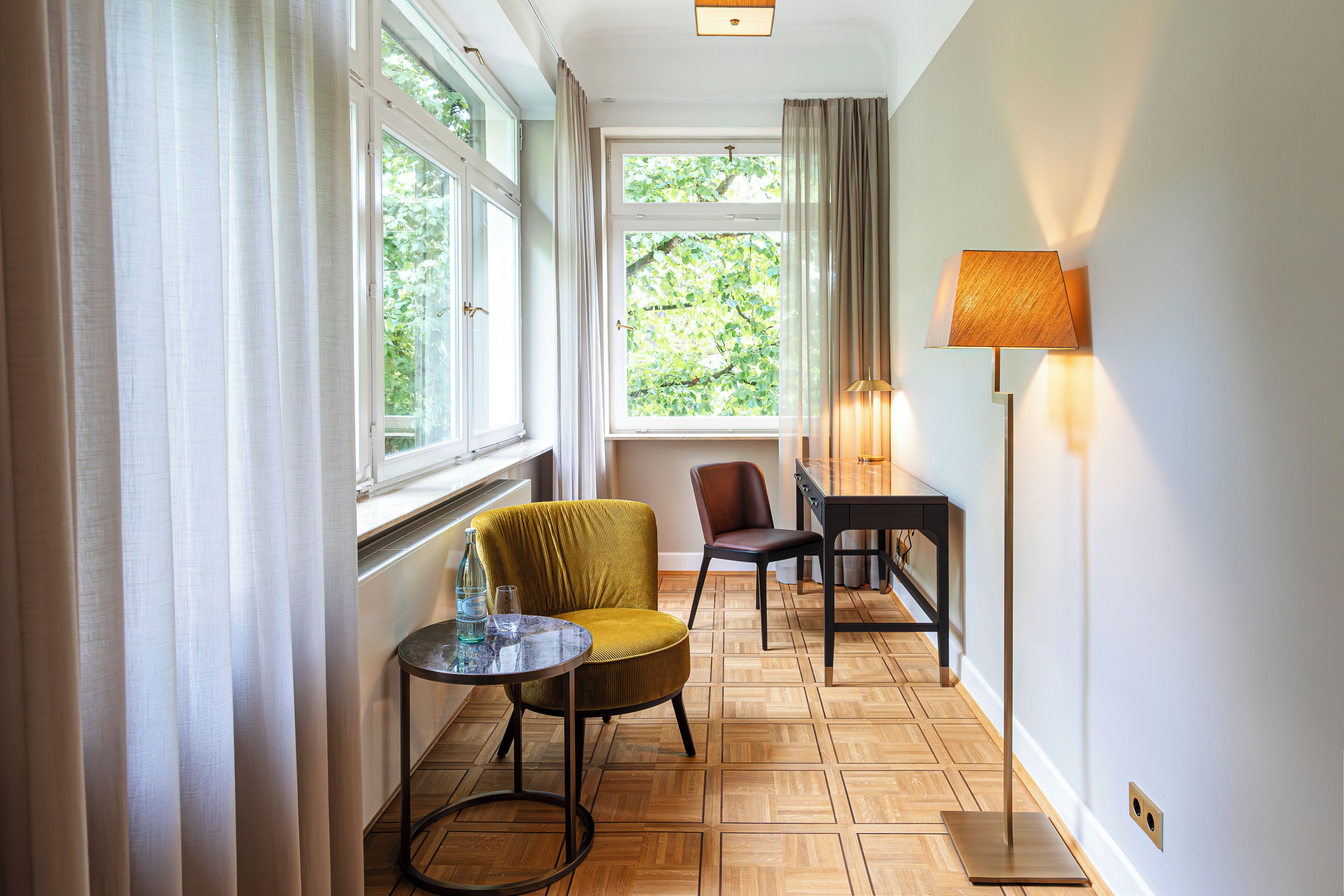 Una habitación con un ventanal grande, una silla, una mesa y una lámpara.