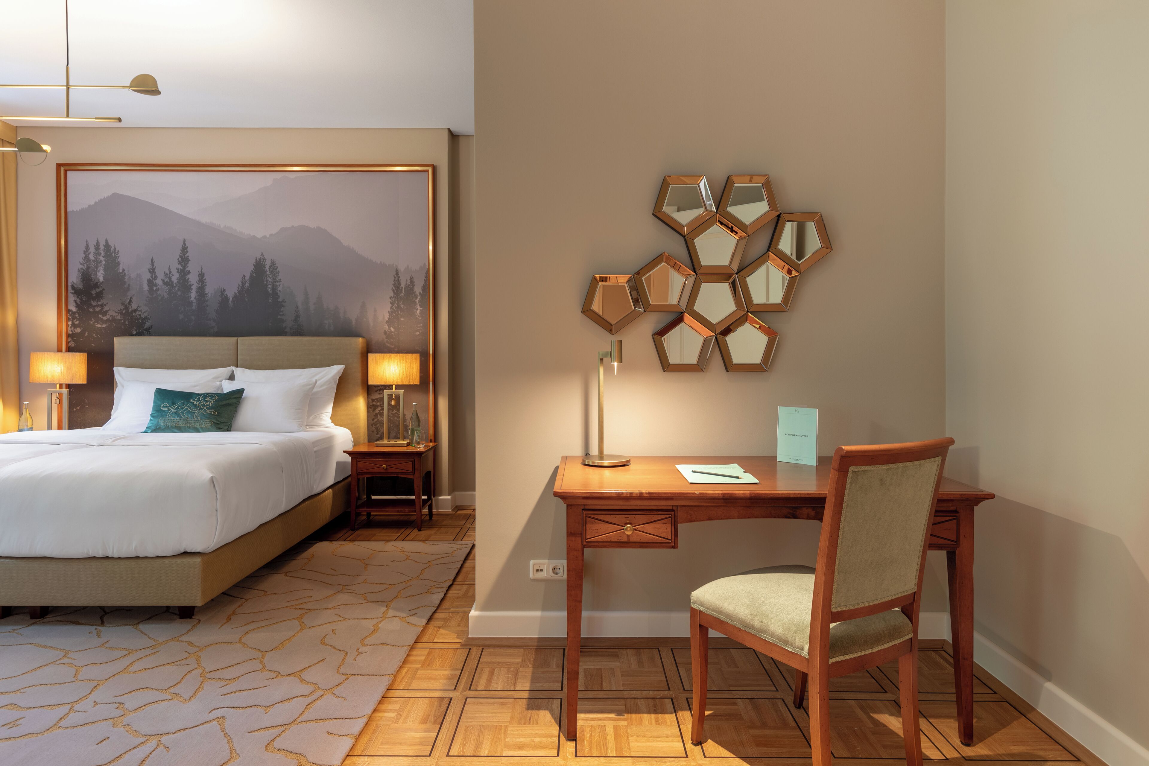 Una habitación de hotel con cama, escritorio, silla y una pared con espejos hexagonales.