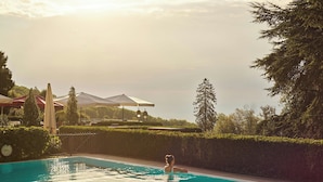 A swimming pool with a person in the water, surrounded by greenery and umbrellas.