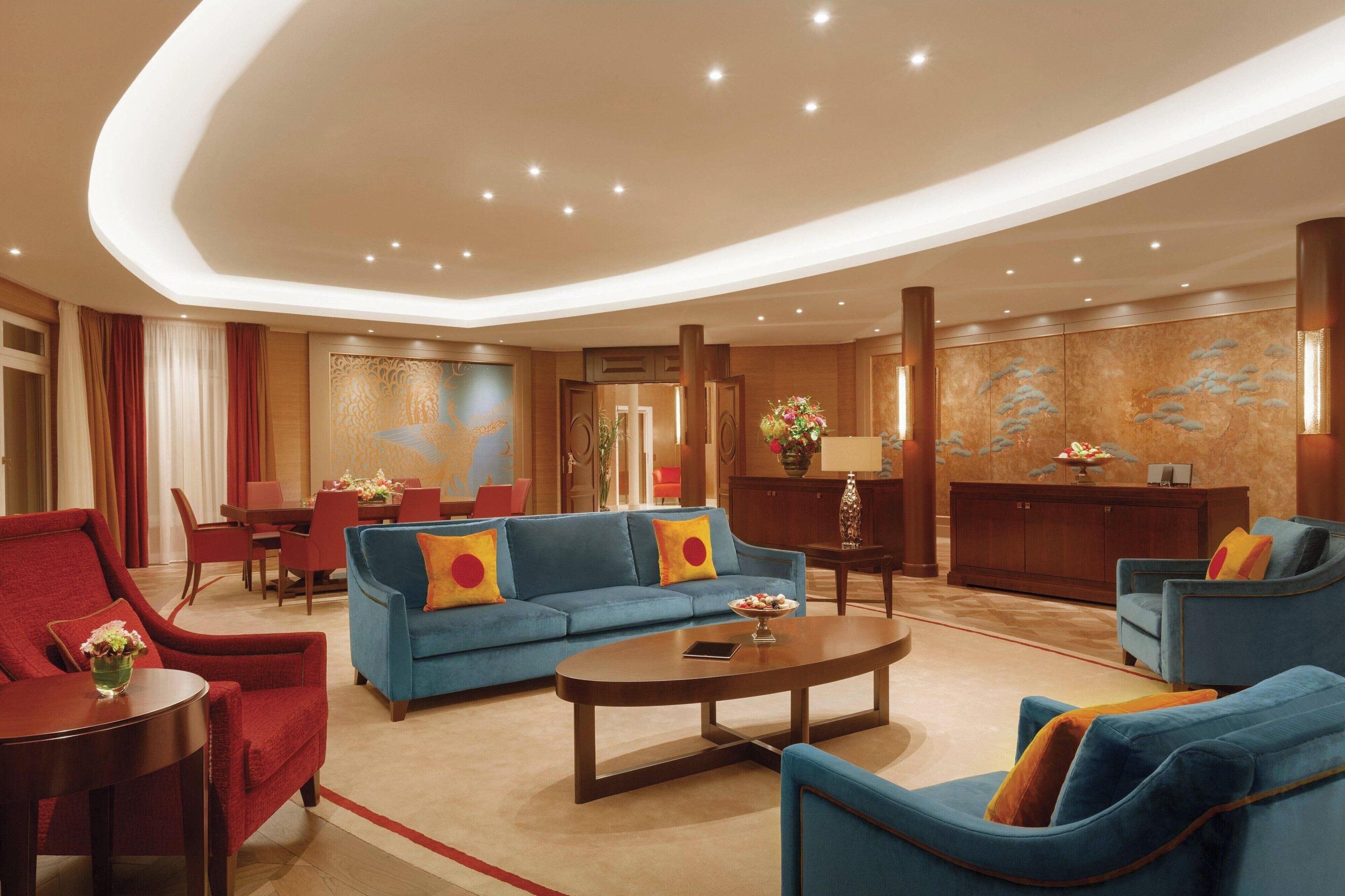 A spacious lobby with a blue sofa, red armchairs, a coffee table, and a dining area.