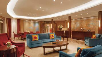 A spacious lobby with a blue sofa, red armchairs, a coffee table, and a dining area.