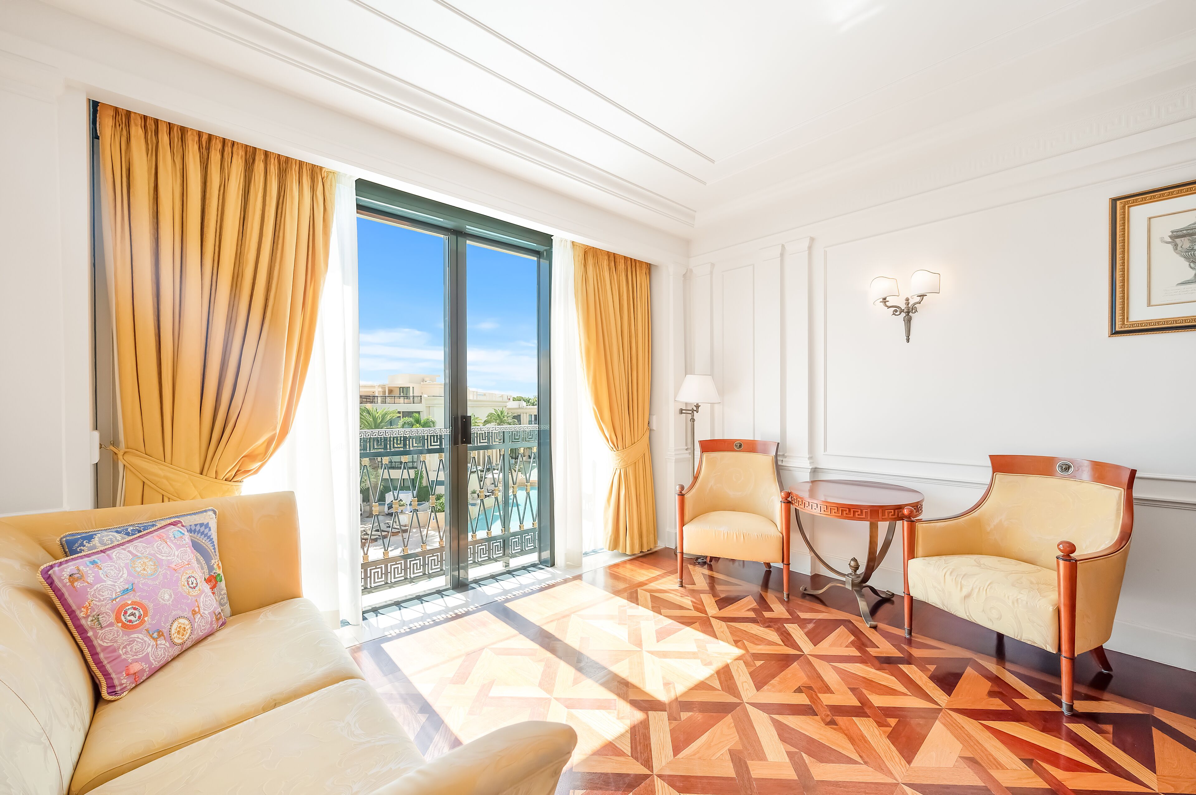 Una habitación de hotel con un gran ventanal corredera, un sofá, dos sillones, una mesita y una lámpara.