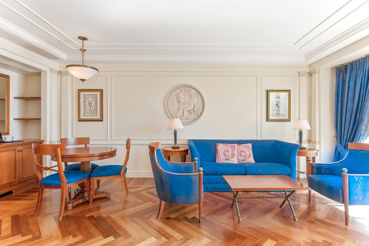 A room with a dining table, blue upholstered chairs, a blue sofa, and a decorative wall piece.