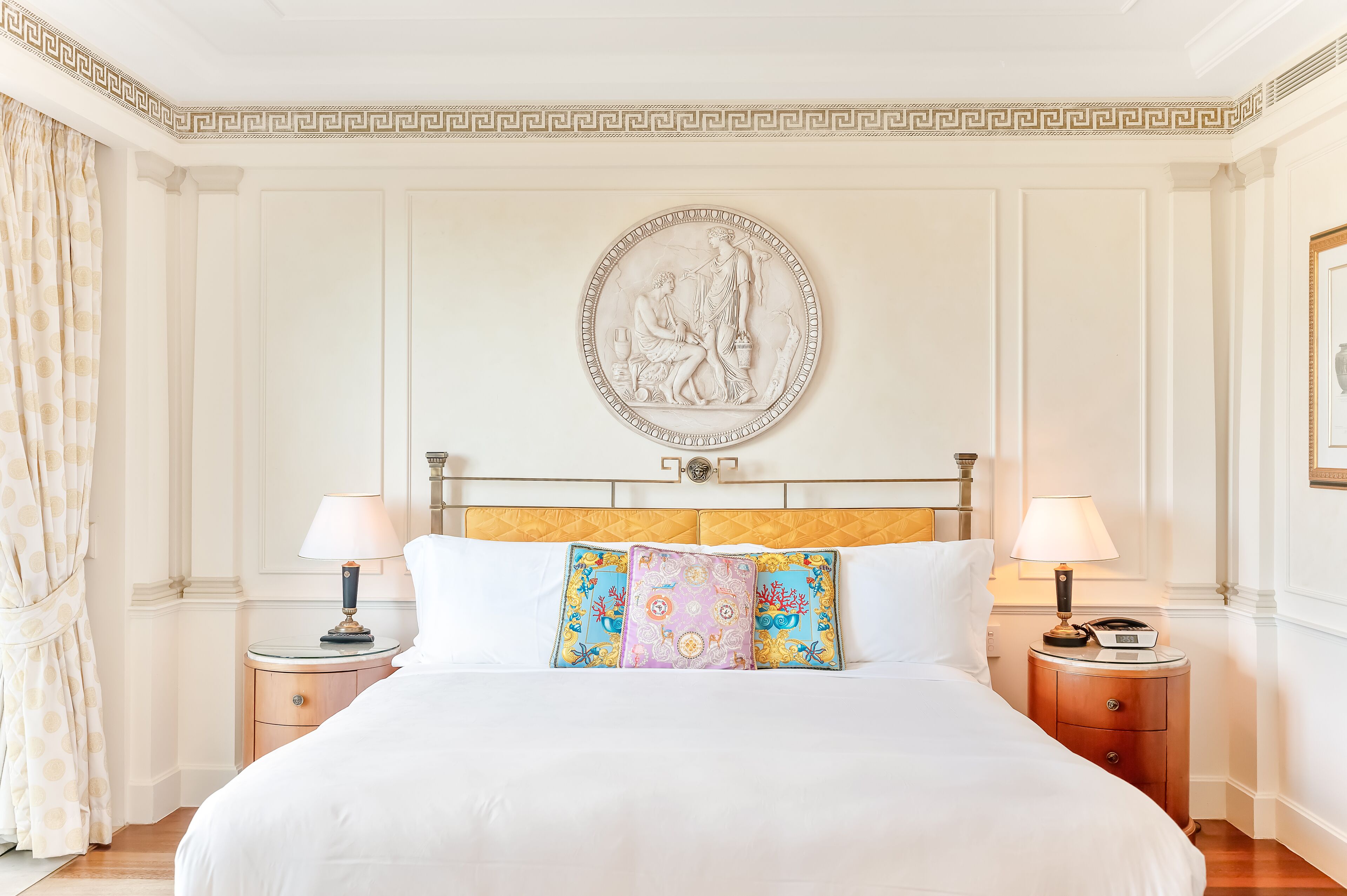 A hotel room with a large bed, two bedside tables with lamps, a decorative wall piece, and a classic headboard.