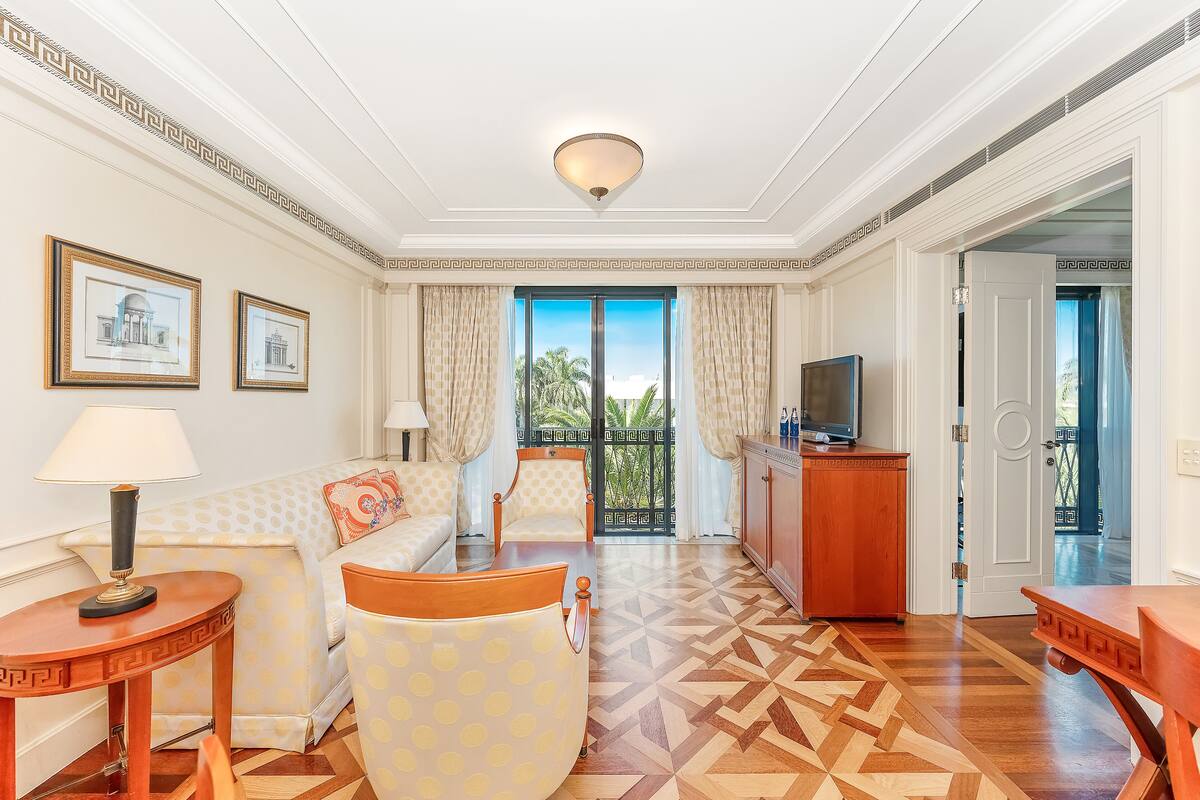 A hotel room with a patterned sofa, a wooden coffee table, a TV, and a view of the outdoors.