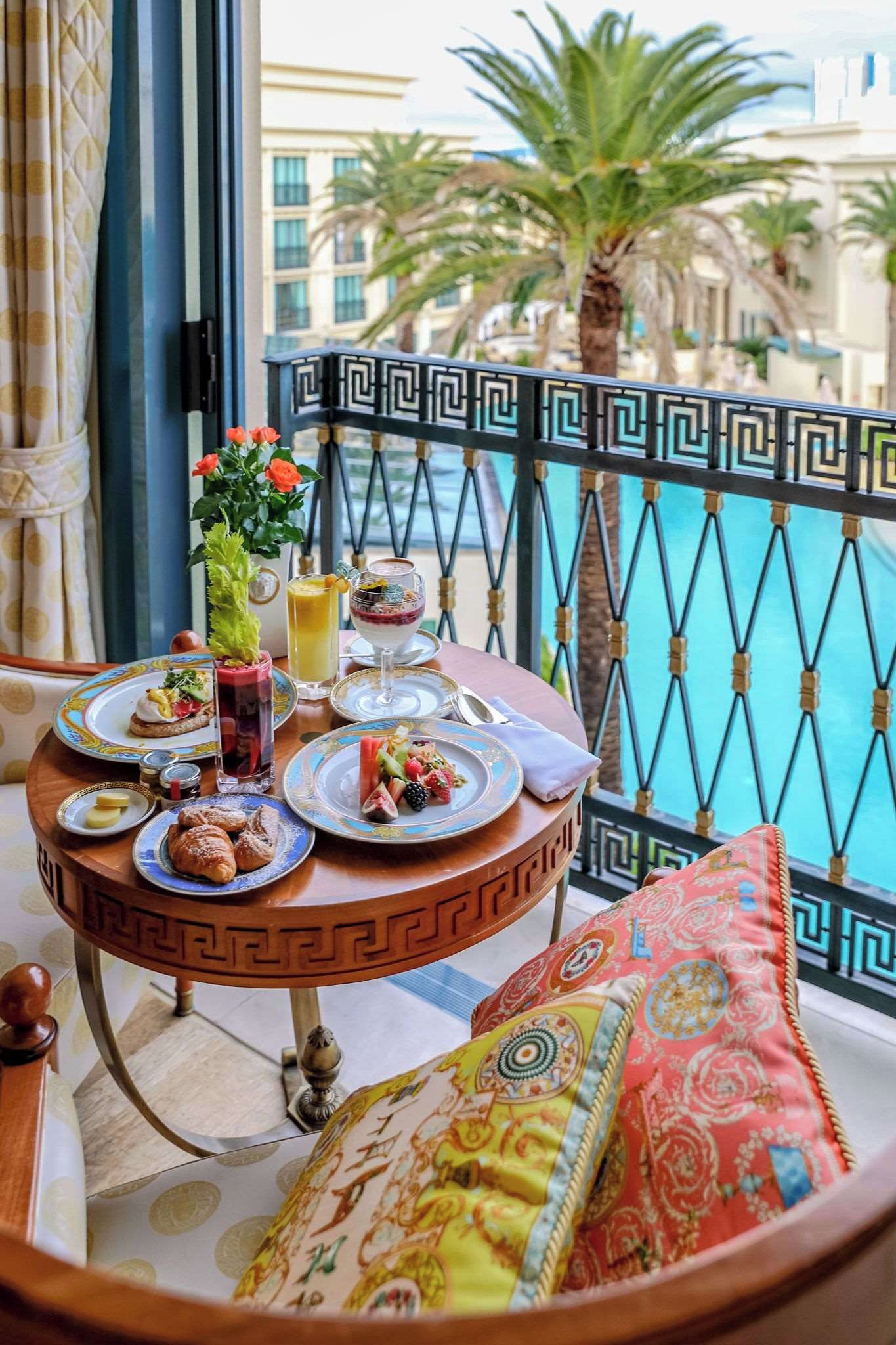 Un balcon avec une table à manger dressée, sur laquelle on trouve des assiettes remplies de nourriture, un verre de jus de fruits et une plante décorative.