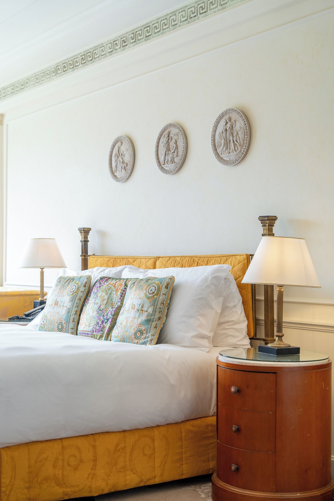 A hotel room with a bed, two bedside lamps, a wooden nightstand, and three wall-mounted decorative plates.
