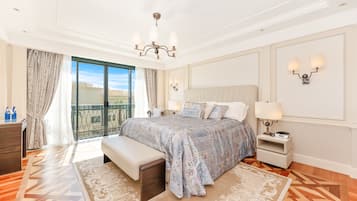 A bedroom with a large bed, a bench, a nightstand, a chandelier, and a view of the outdoors.