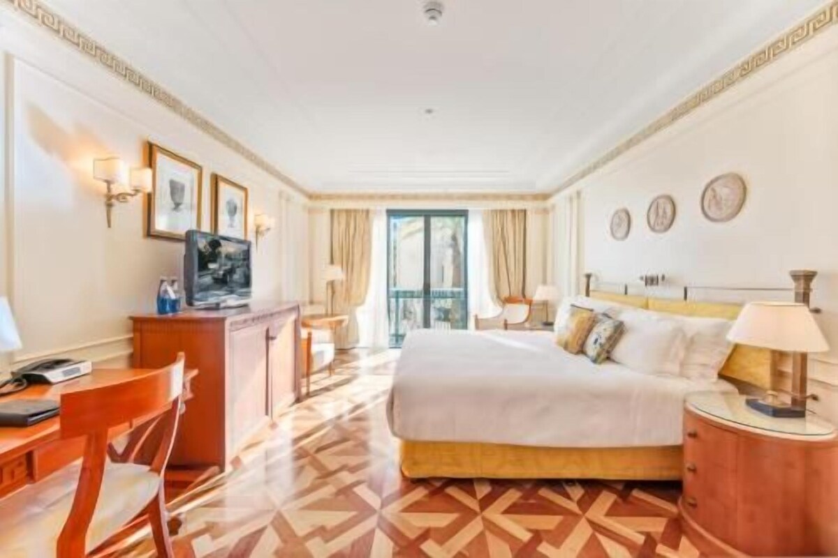 A hotel room with a bed, a desk, a chair, a TV, and a window with curtains.