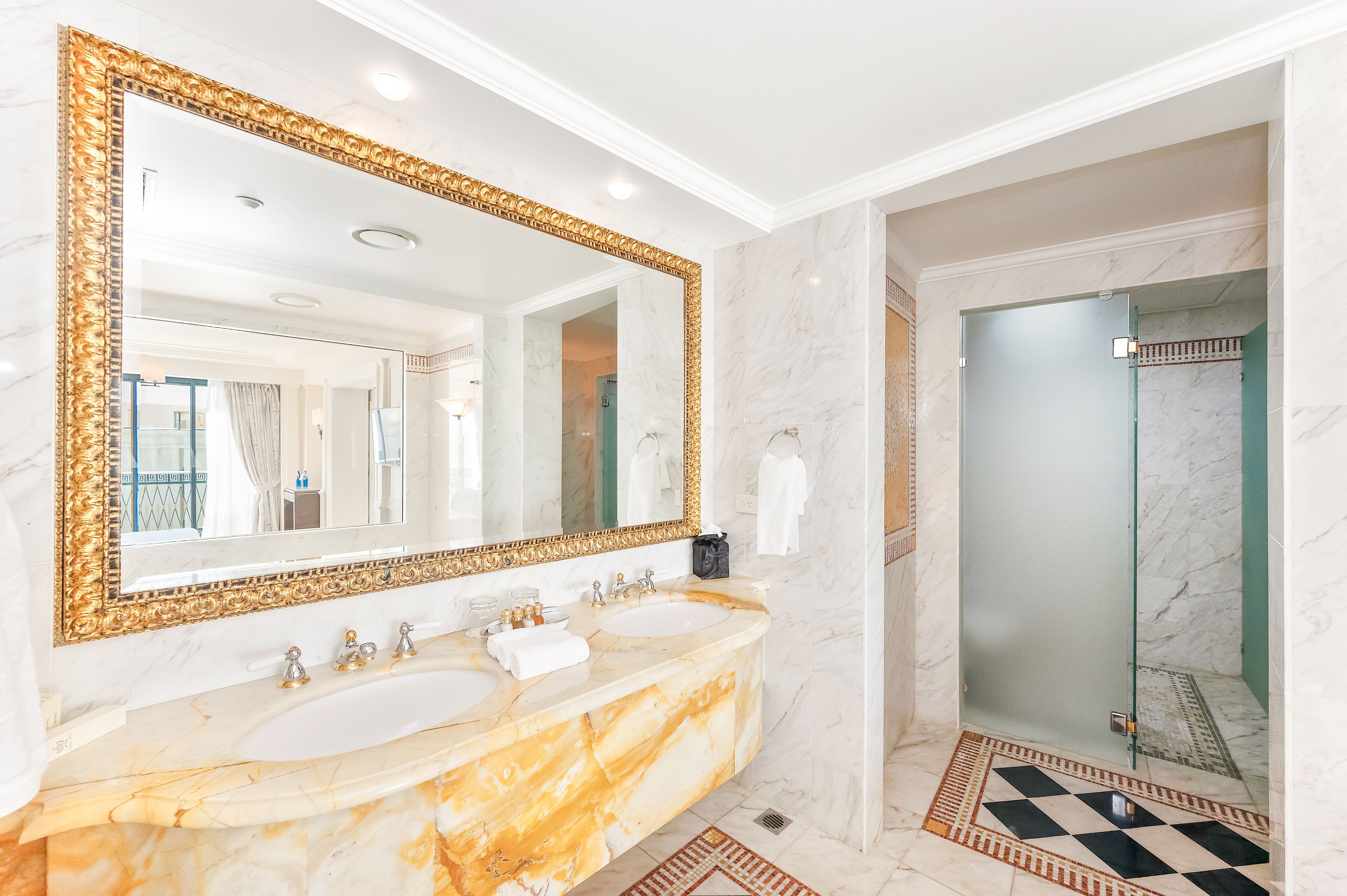 Un bagno con due lavandini, un ampio specchio con cornice dorata e cabina doccia in vetro.