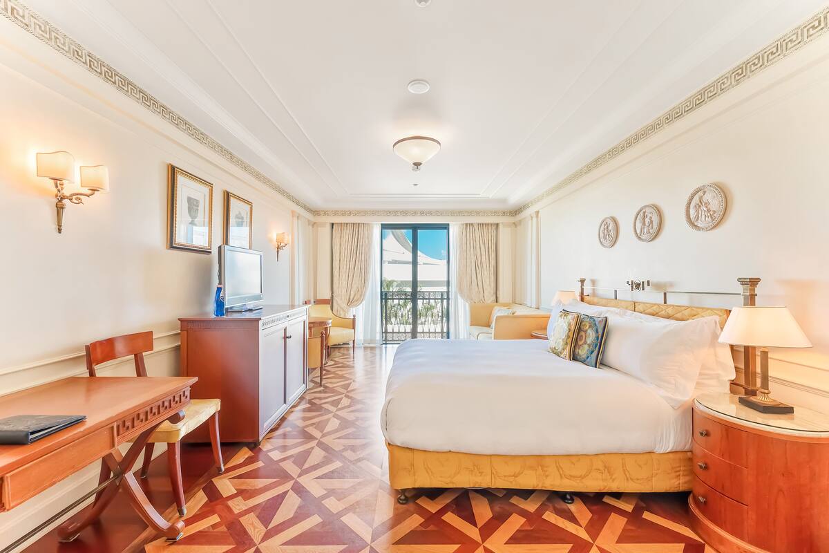 A hotel room with a bed, a desk, a chair, a TV, and a view of the outdoors.