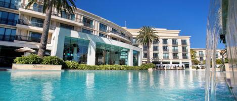 A hotel with a large swimming pool, palm trees, and modern architecture.