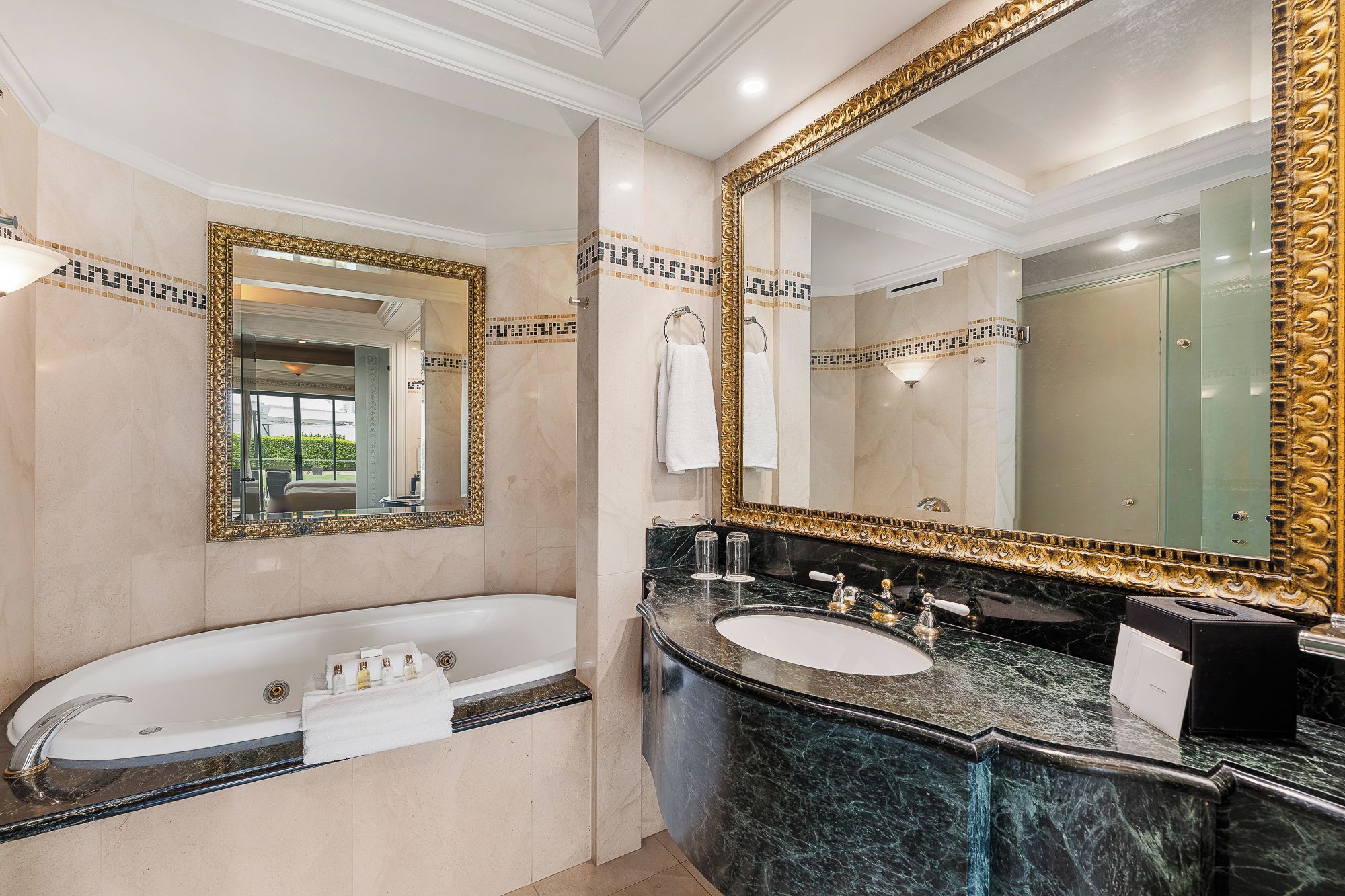 Un baño lujoso con una bañera independiente grande, un tocador doble y dos espejos amplios con marcos dorados ornamentados.