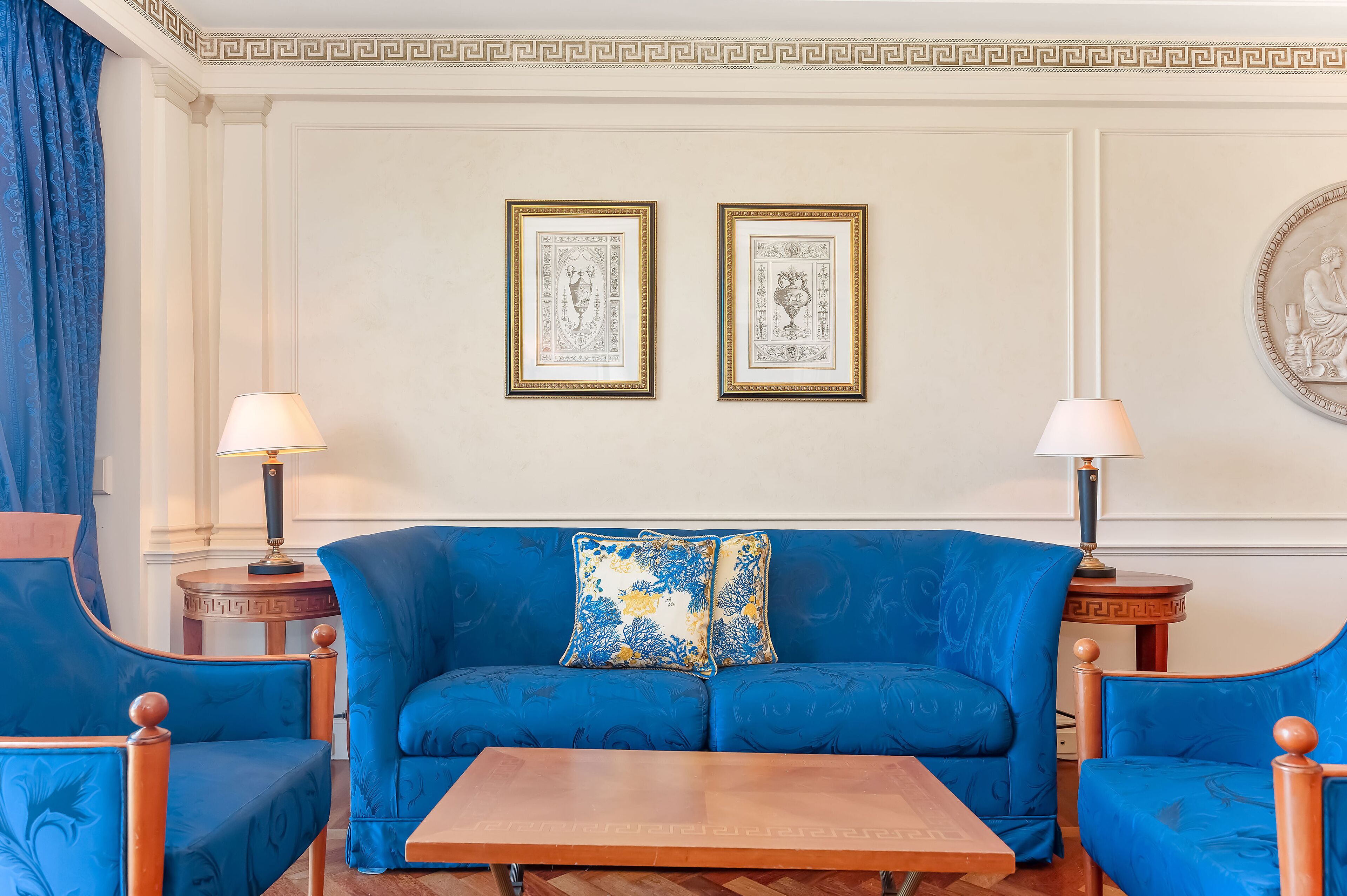 A room with a blue sofa, two armchairs, a wooden coffee table, and two lamps.