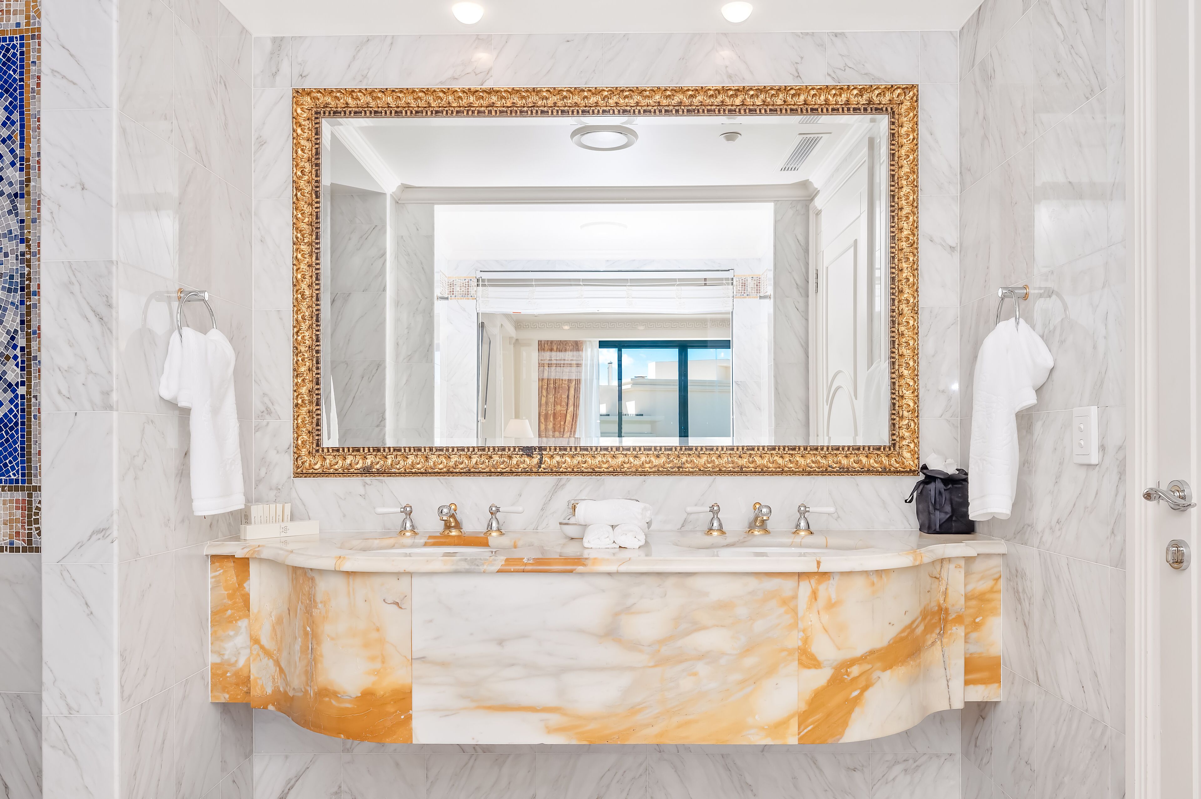 Un baño con un espejo grande, tocador de mármol y dos percheros para toallas.