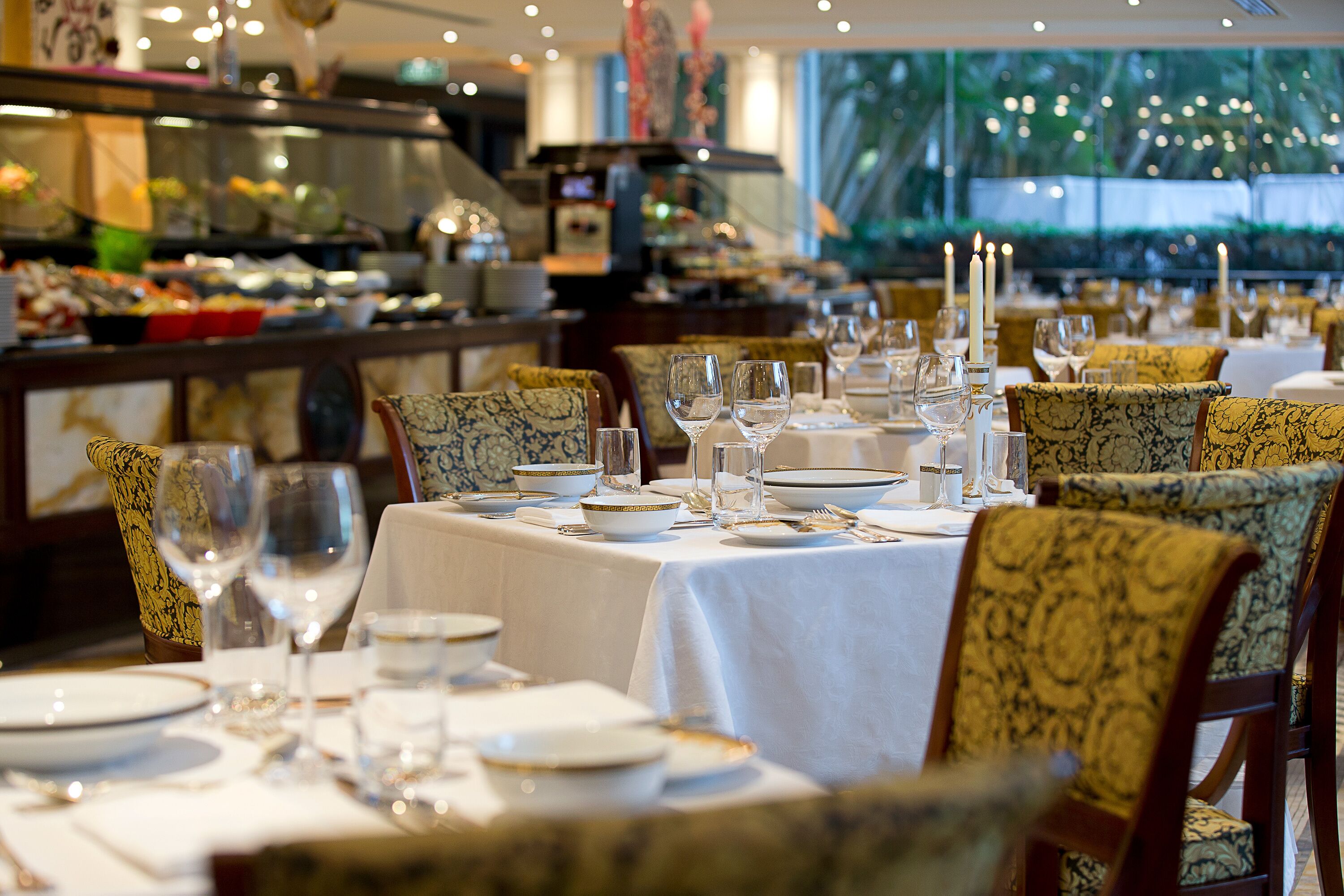 Un restaurante con varias mesas dispuestas para comer, con manteles blancos y platos con borde dorado.