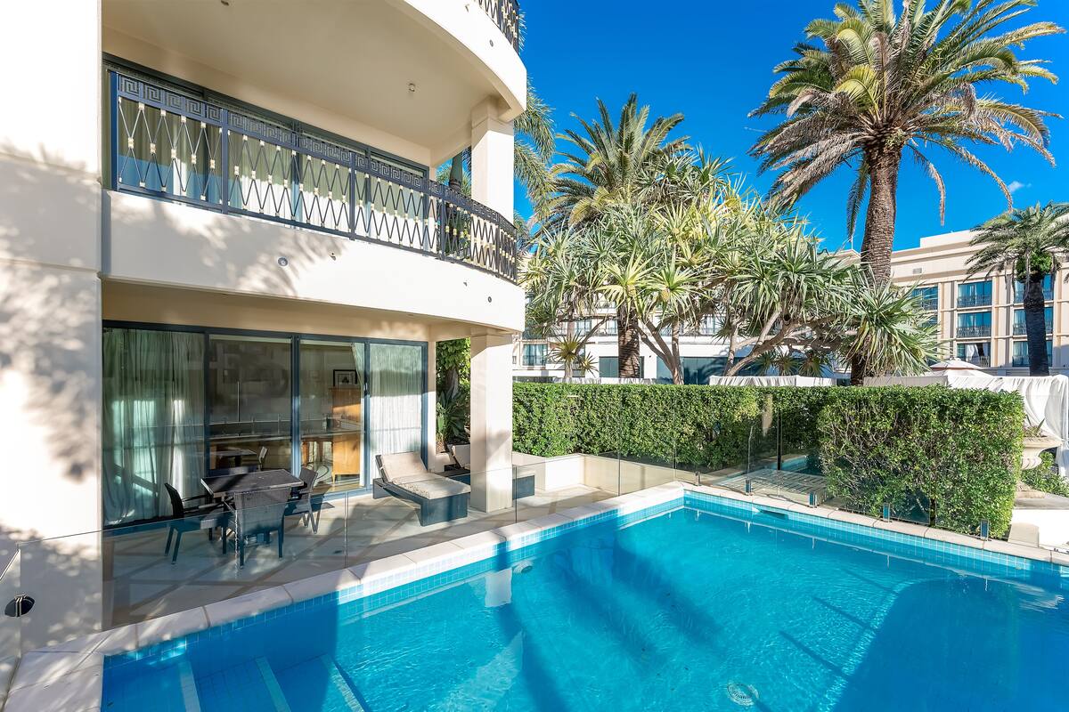 A modern hotel with a swimming pool, outdoor seating, and palm trees.