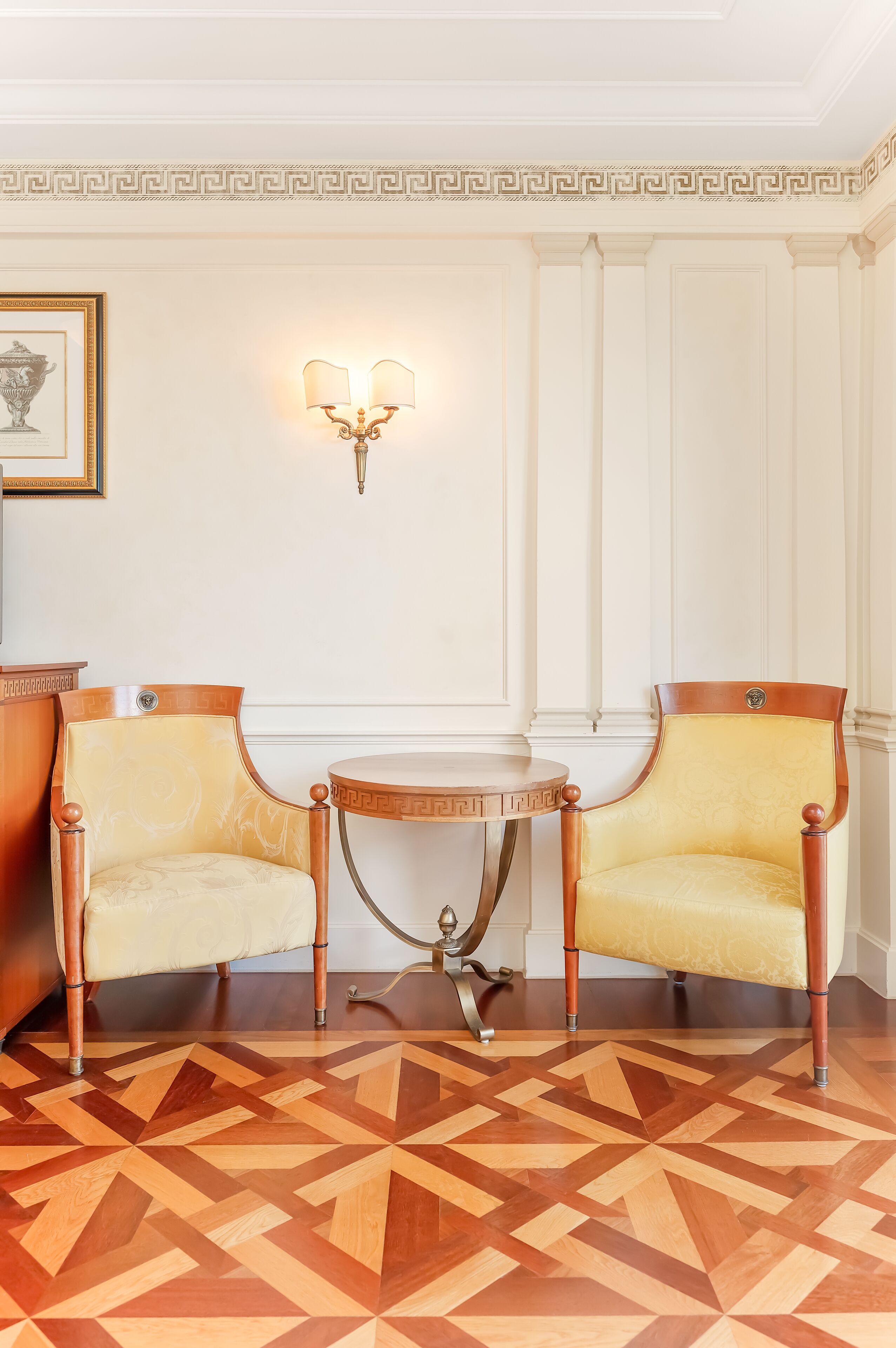 A room with two armchairs, a small table, a wall-mounted light fixture, and a patterned floor.