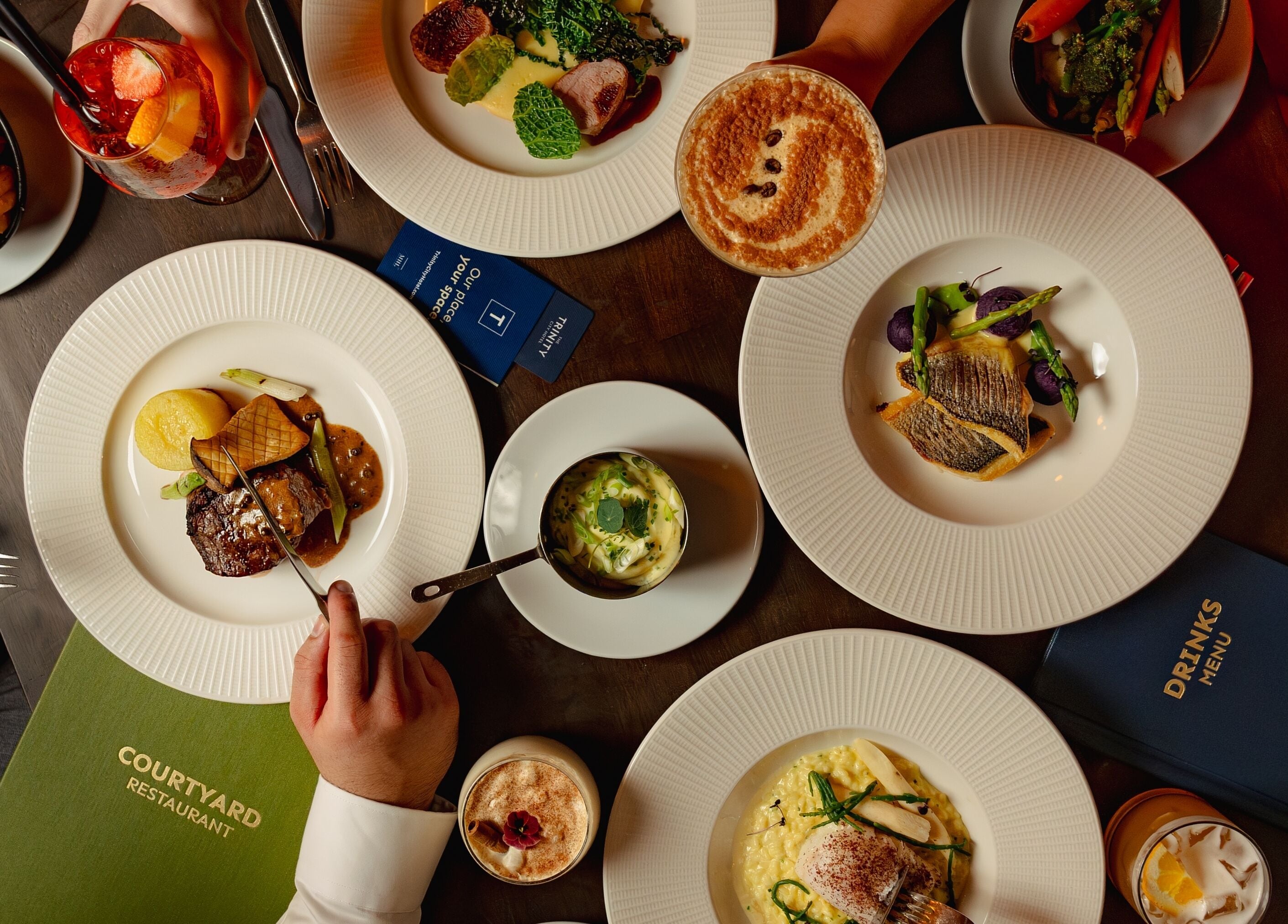 Una mesa servida con diversos platos, incluyendo un bistec, verduras y un postre. Se observan platos, cubiertos y una carta.