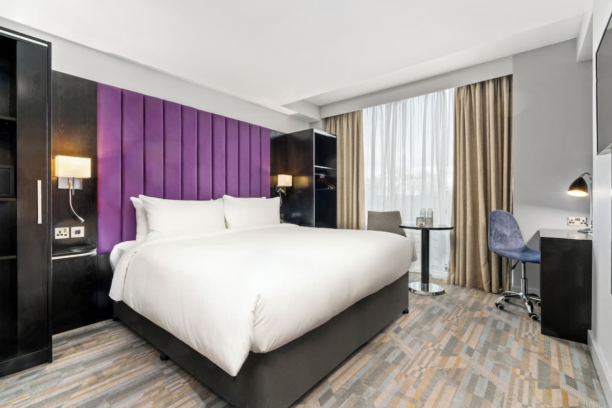 Hotellihuone, jossa on suuri sänky, työpöytä, tuoli, vaatekaappi ja ikkuna, jossa on verhot.