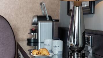 A hotel room with a coffee machine, two coffee cups labeled 'The Trinity City Hotel,' and two croissants on a plate.