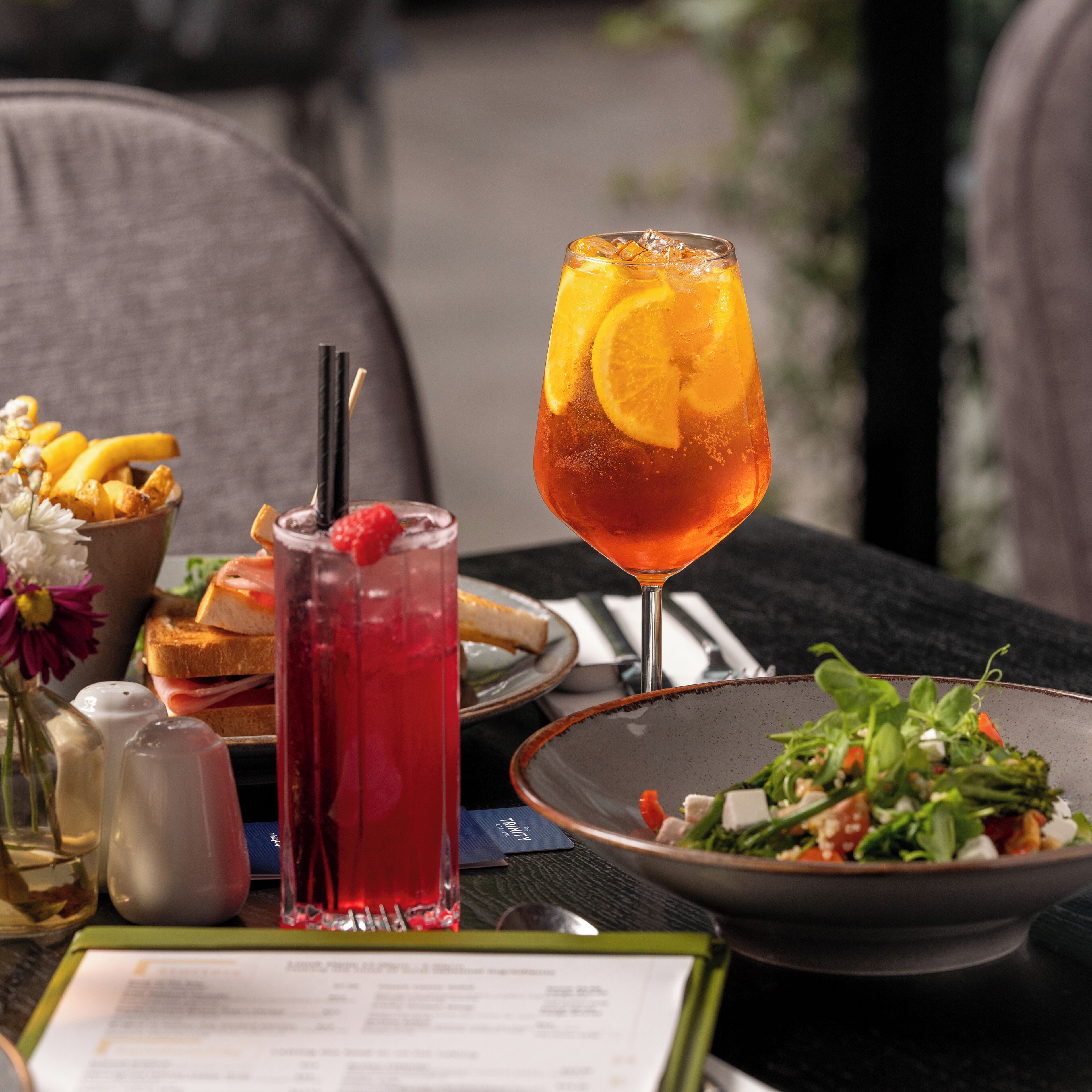 A table with a meal, a drink with an orange slice, and a menu.