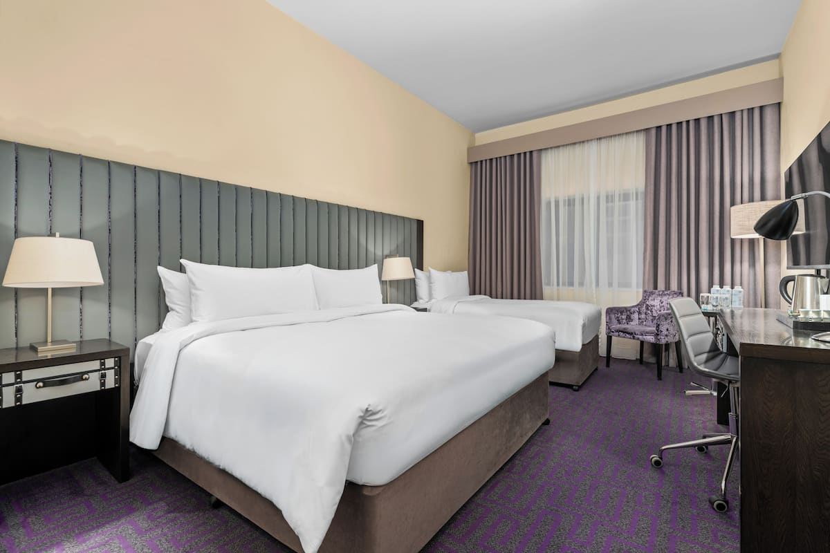 Hotellihuone, jossa on kaksi sänkyä, työpöytä, tuoli, lamppu ja ikkuna, jossa on verhot.