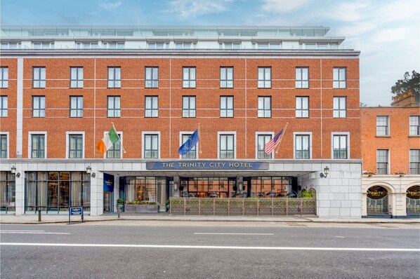 Un hotel con fachada de ladrillo, múltiples ventanas y banderas, incluyendo las de Irlanda y la Unión Europea.