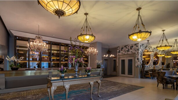 Un vestíbulo espacioso con candelabros ornamentales, una recepción y un amplio ventanal con vistas al interior.