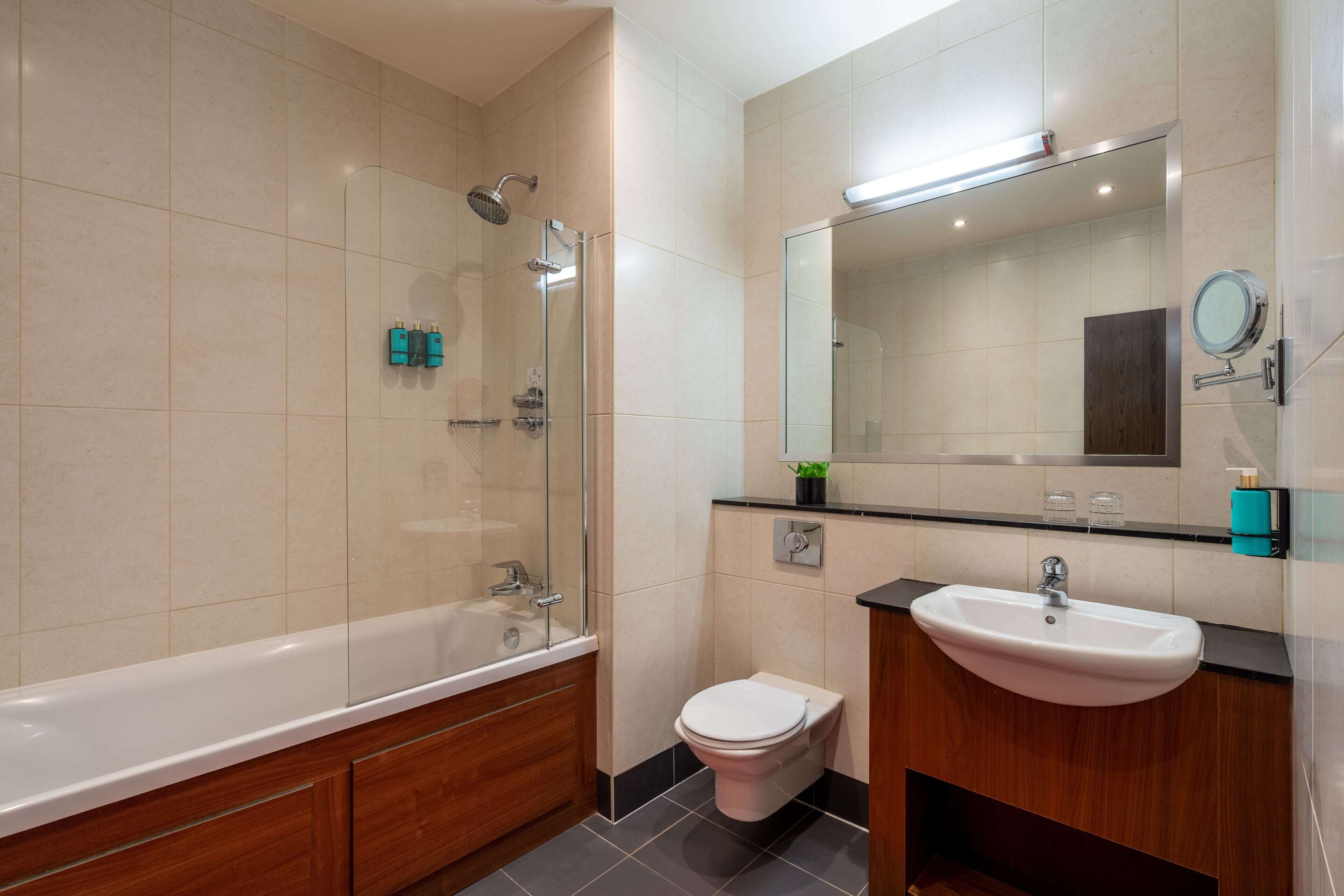 Un baño moderno con ducha envuelta en vidrio, inodoro blanco y tocador de madera con lavabo.