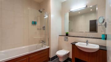Un baño moderno con ducha envuelta en vidrio, inodoro blanco y tocador de madera con lavabo.
