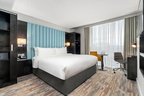 A hotel room with a large bed, a desk, a chair, a TV, and a window with curtains.